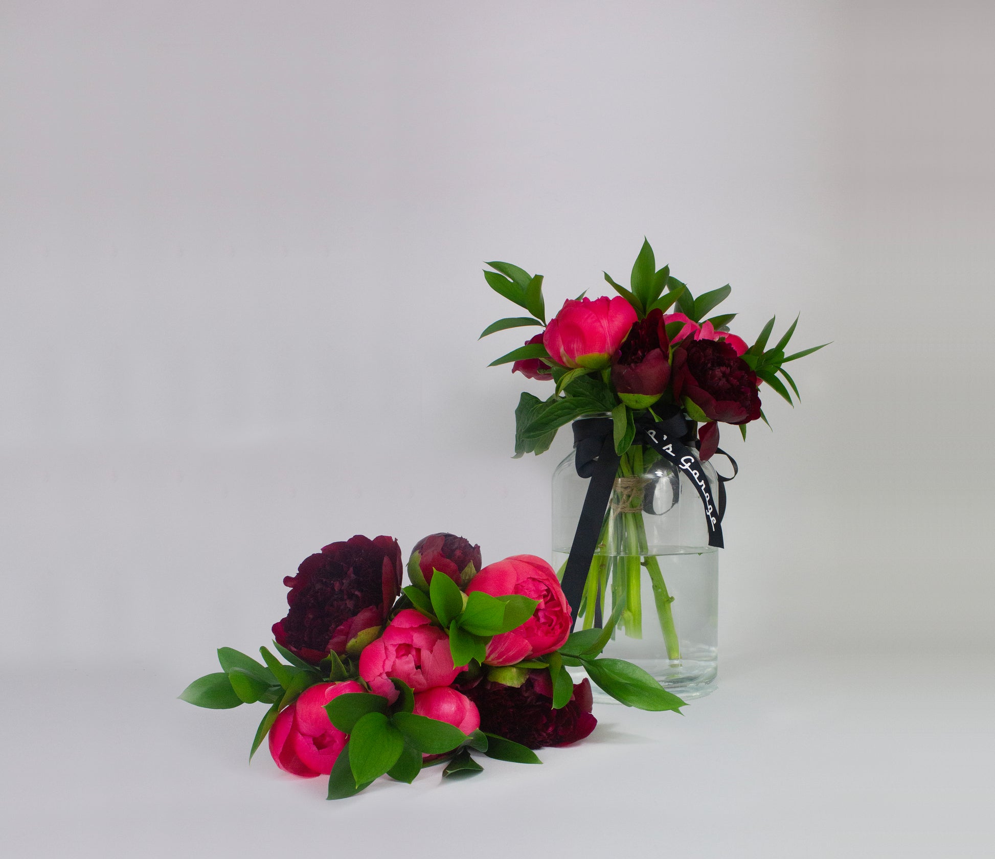 Bouquets of pink and dark red flowers with green leaves in a clear glass vase on a white background